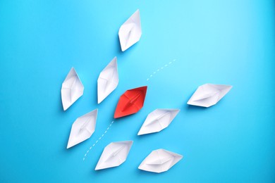 Photo of Red paper boat floating between others on light blue background, flat lay. Uniqueness concept