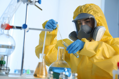 Scientist in chemical protective suit dripping reagent  into test tube at laboratory. Virus research