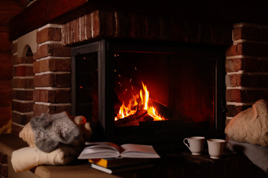 Photo of Knitwear and books near fireplace with burning wood indoors. Winter vacation