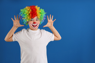 Photo of Preteen boy with clown makeup and wig on blue background, space for text. April fool's day