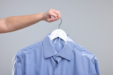 Photo of Dry-cleaning service. Woman holding shirt in plastic bag on gray background, closeup