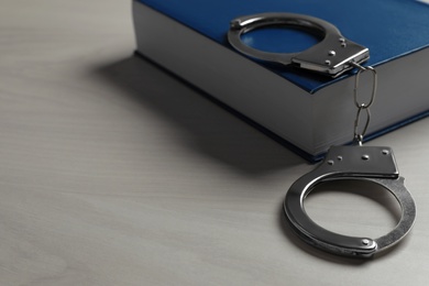 Handcuffs and book on white wooden background, space for text. Criminal law concept