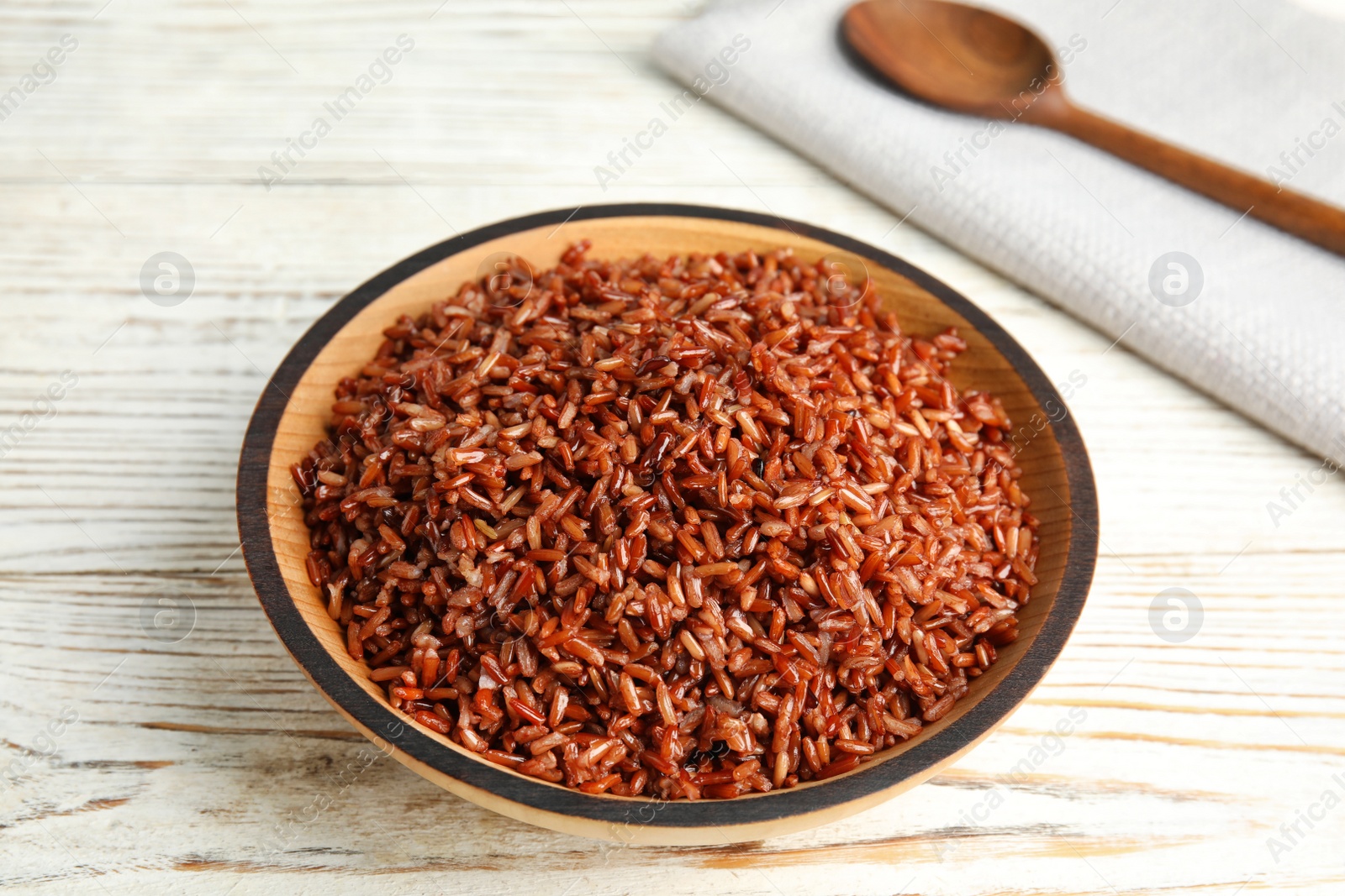 Photo of Bowl with delicious cooked brown rice on white wooden table