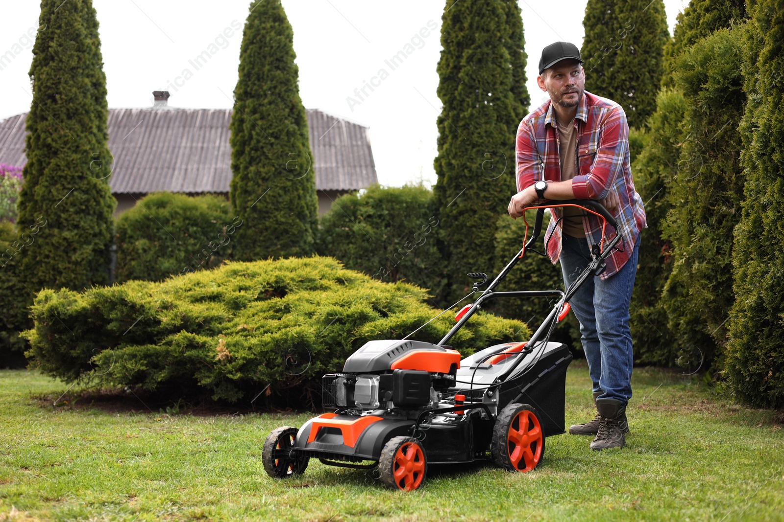 Photo of Man cutting green grass with lawn mower in garden