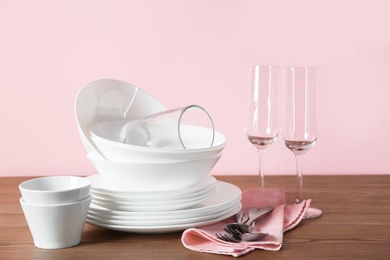 Set of clean dishes and glasses on table against color background