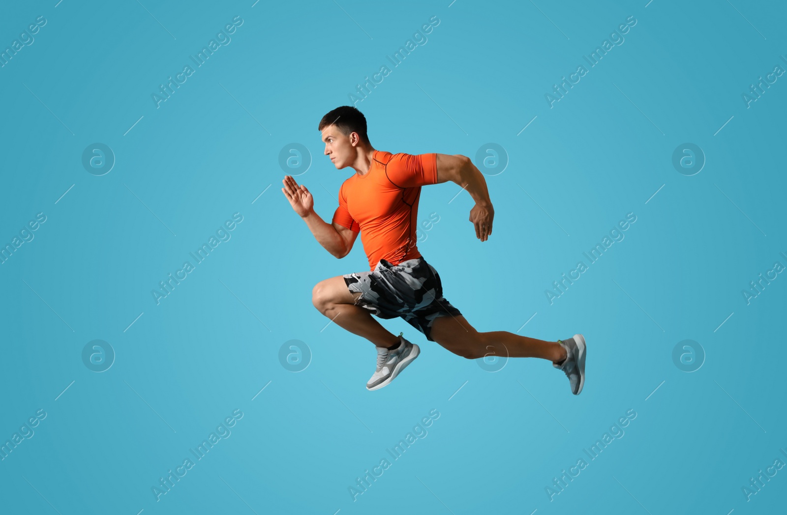 Photo of Athletic young man running on light blue background, side view