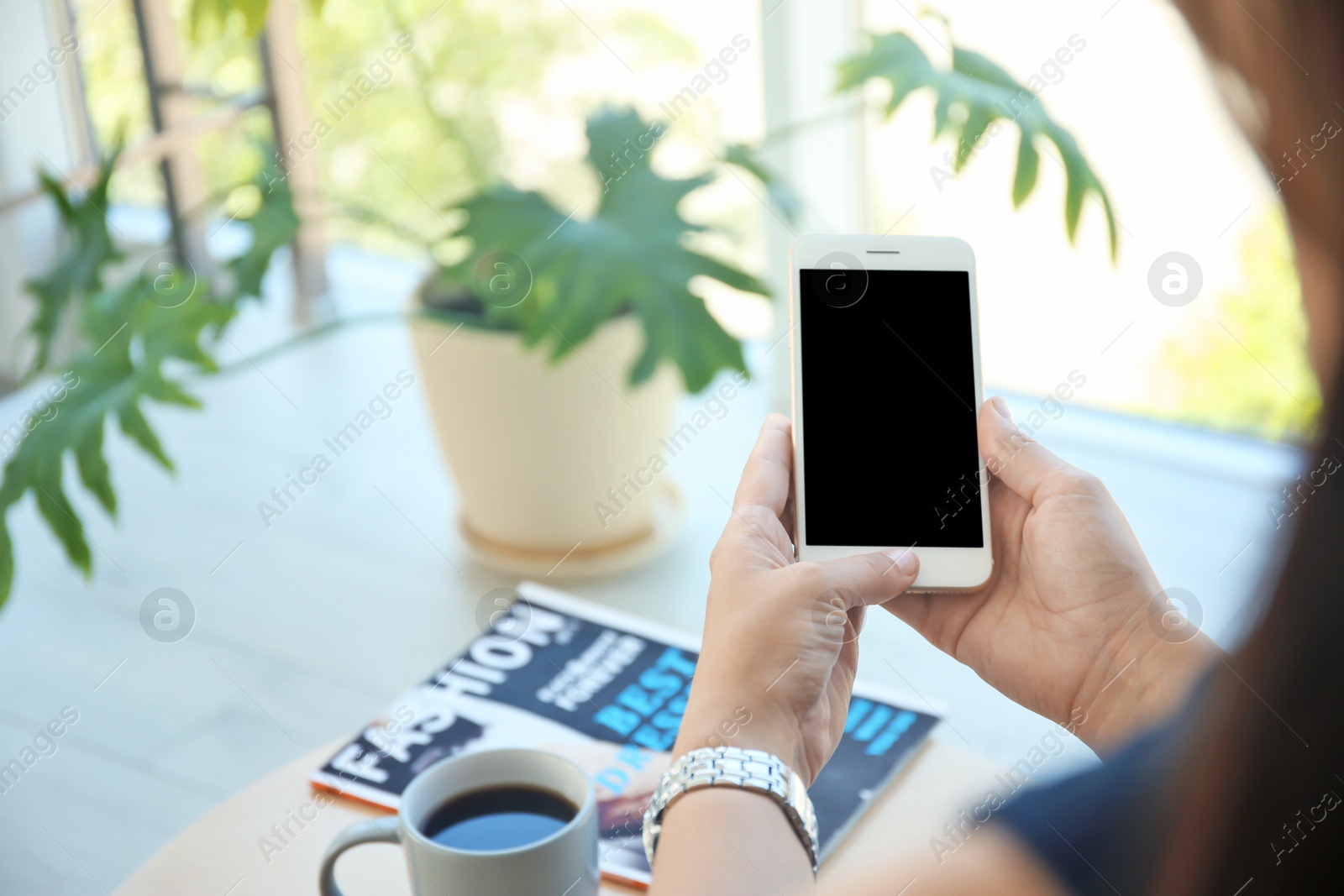 Photo of Young woman holding mobile phone with blank screen in hands indoors