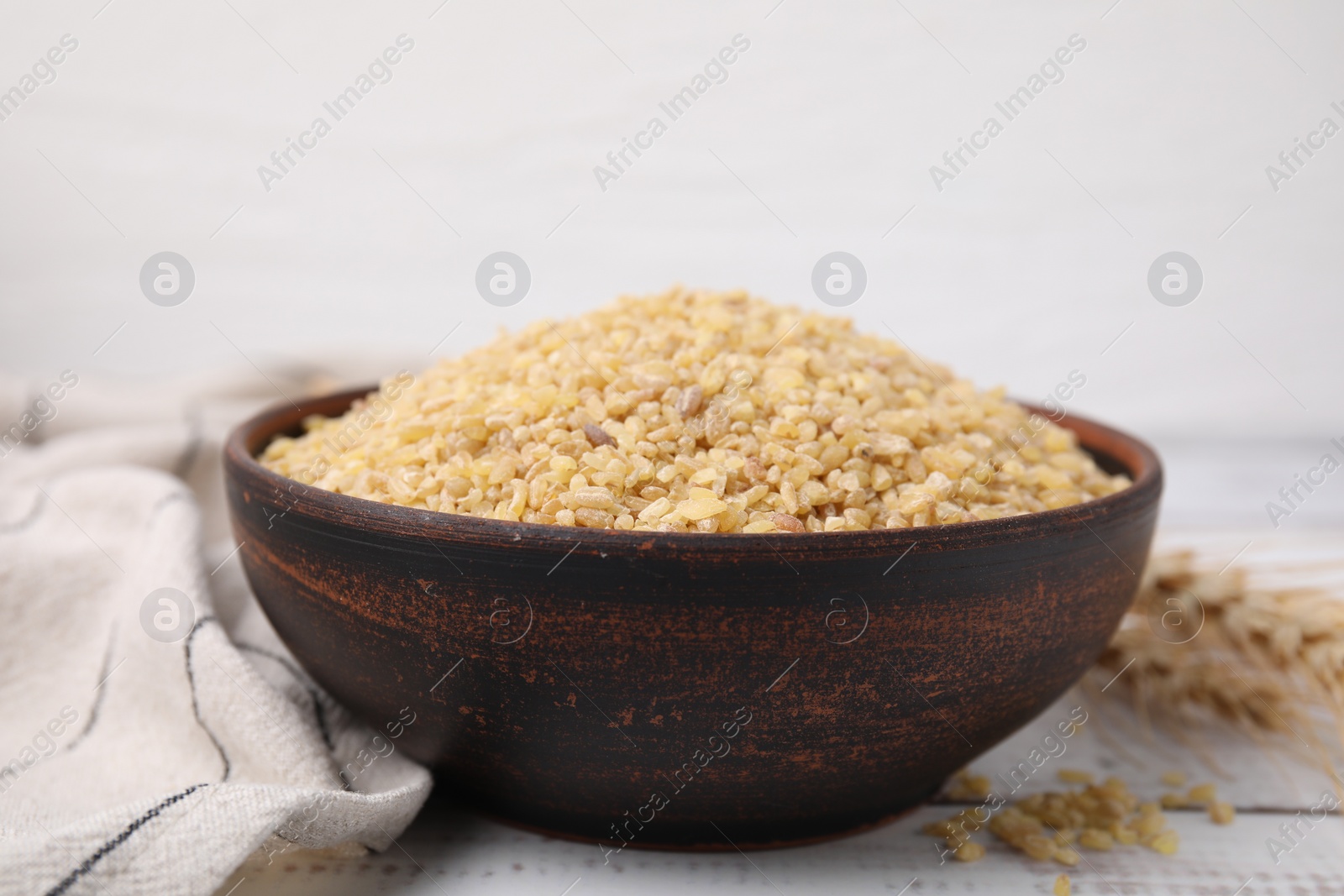 Photo of Raw bulgur in bowl on white wooden table, closeup