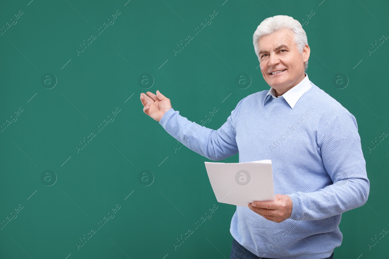 Photo of Portrait of senior teacher with paper at green chalkboard, space for text