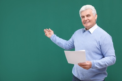 Photo of Portrait of senior teacher with paper at green chalkboard, space for text