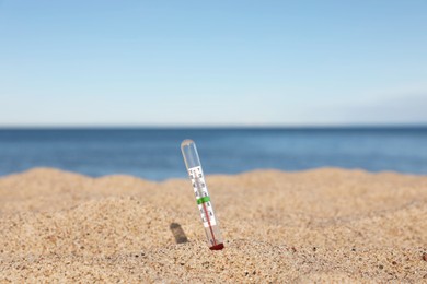 Weather thermometer in sand near sea, space for text