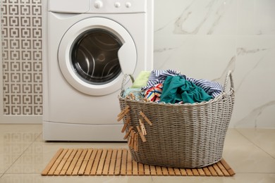 Photo of Wicker basket with dirty clothes on floor in laundry room