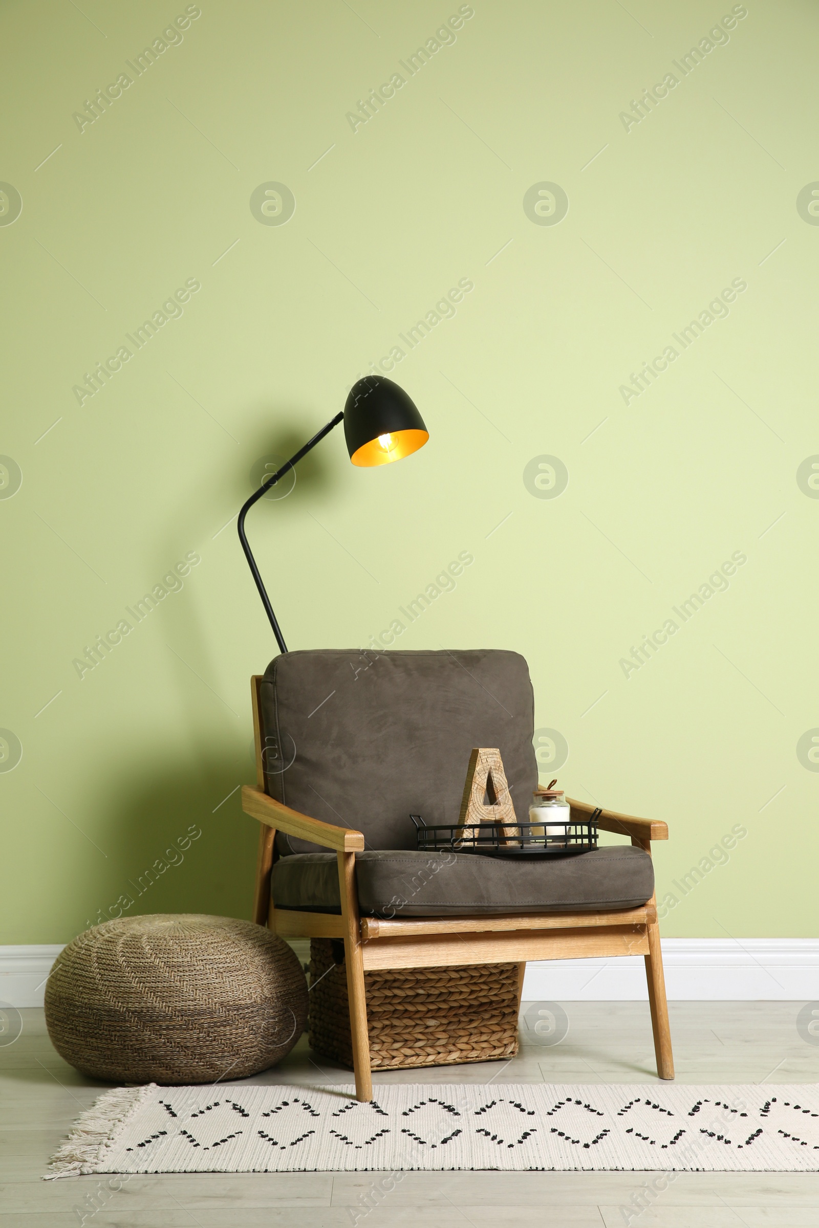 Photo of Stylish room interior with comfortable knitted pouf and armchair near light green wall