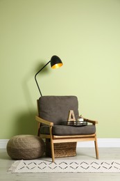 Photo of Stylish room interior with comfortable knitted pouf and armchair near light green wall