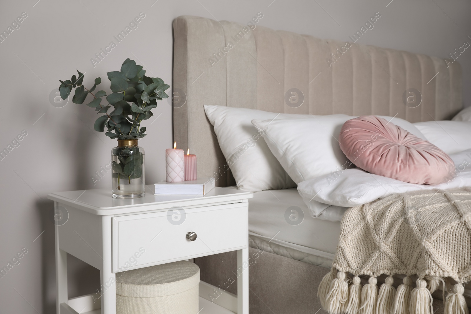 Photo of Vase with beautiful eucalyptus branches, book and candles on nightstand in bedroom