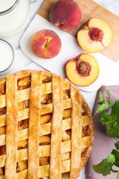 Photo of Delicious peach pie and fresh fruits on white marble table, flat lay