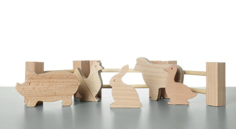 Photo of Set of wooden animals and fence on light grey table against white background. Children's toy