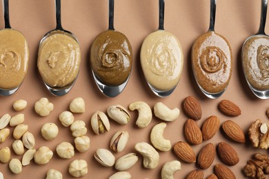 Photo of Tasty nut butters in spoons and raw nuts on light brown table, flat lay