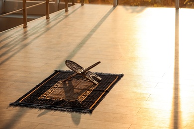 Photo of Rehal on Muslim prayer mat indoors. Space for text