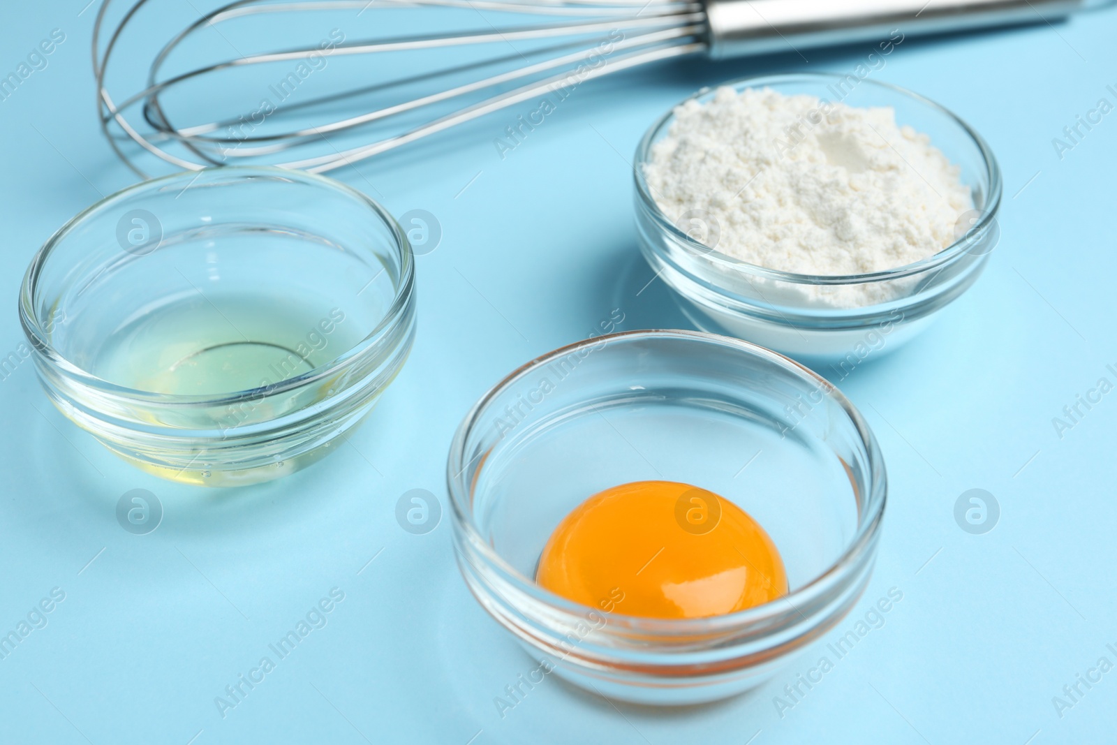 Photo of Egg yolk, white and flour in bowls on light blue background, closeup