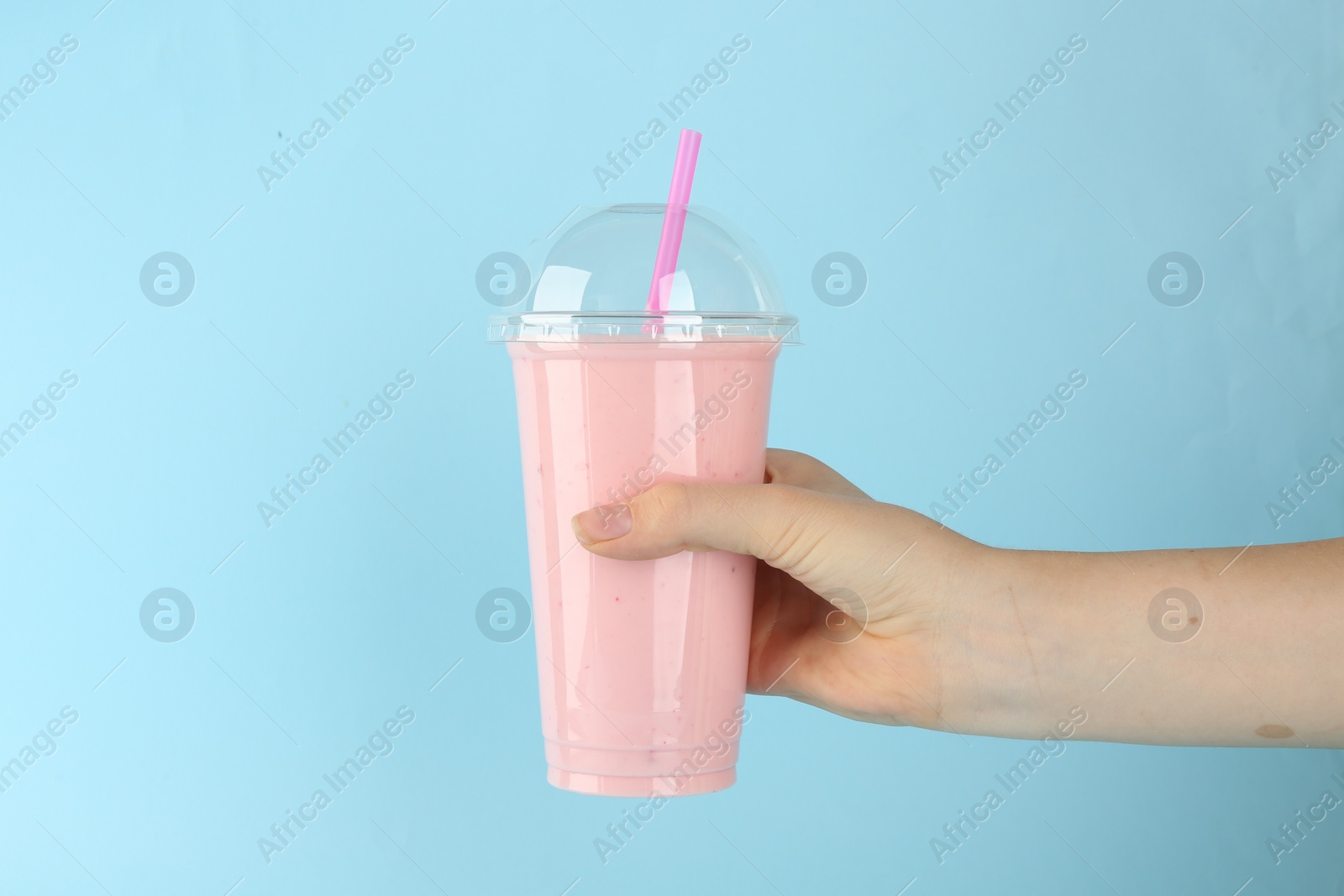 Photo of Woman with plastic cup of tasty smoothie on light blue background, closeup