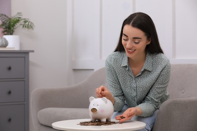 Photo of Young woman putting coin into piggy bank at home