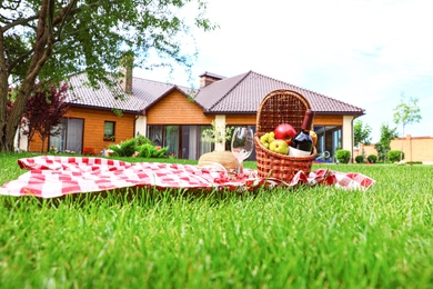 Picnic basket with fruits and bottle of wine on checkered blanket in garden