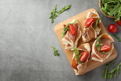 Photo of Tasty sandwiches with cured ham, tomatoes and arugula on grey table, flat lay. Space for text