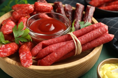 Photo of Different thin dry smoked sausages, parsley and sauces on green wooden table, closeup