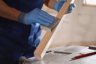 Photo of Professional carpenter polishing wooden bar in workshop, closeup