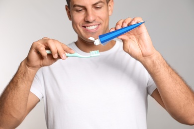 Photo of Man applying toothpaste on brush against light background