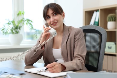 Smiling secretary talking on telephone at table in office