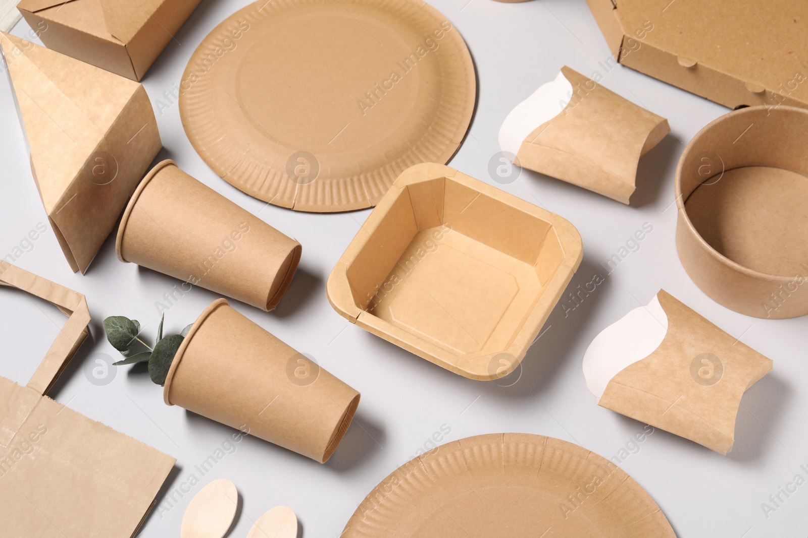 Photo of Eco friendly food packaging. Paper containers, tableware and eucalyptus leaves on light grey background