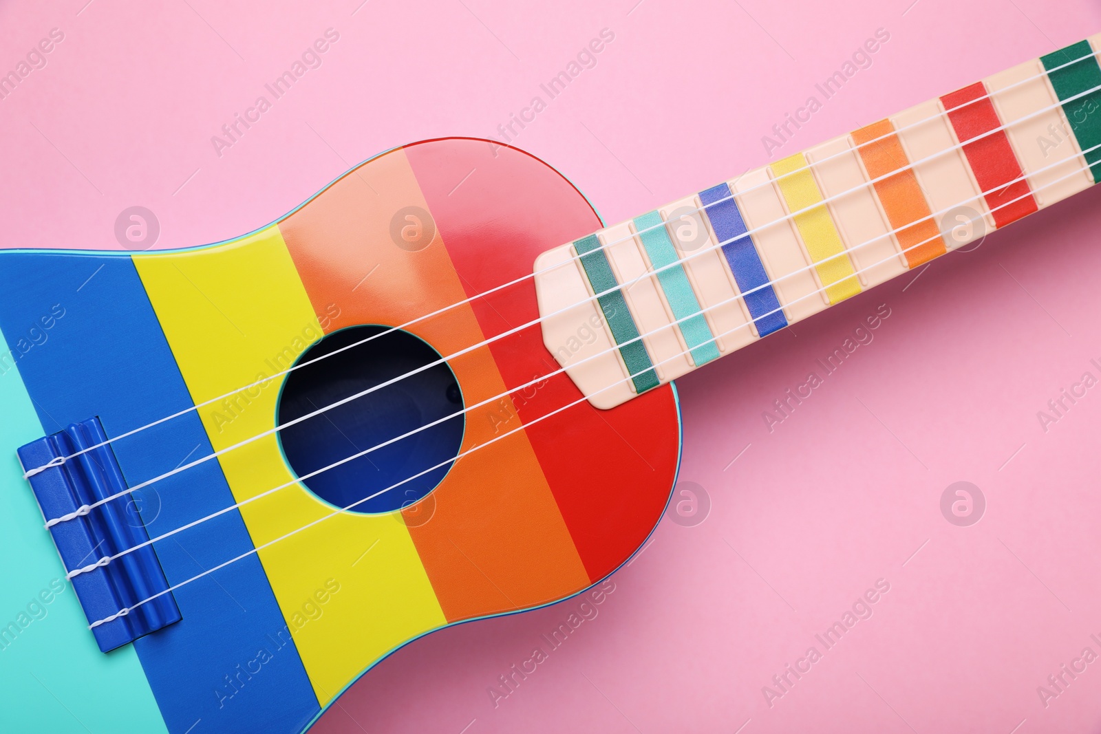 Photo of Colorful ukulele on pink background, top view. String musical instrument