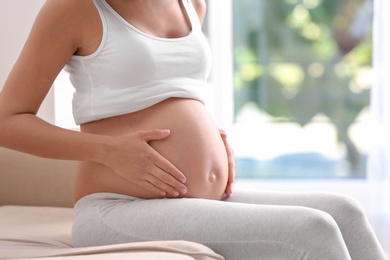 Pregnant woman sitting on sofa at home, closeup