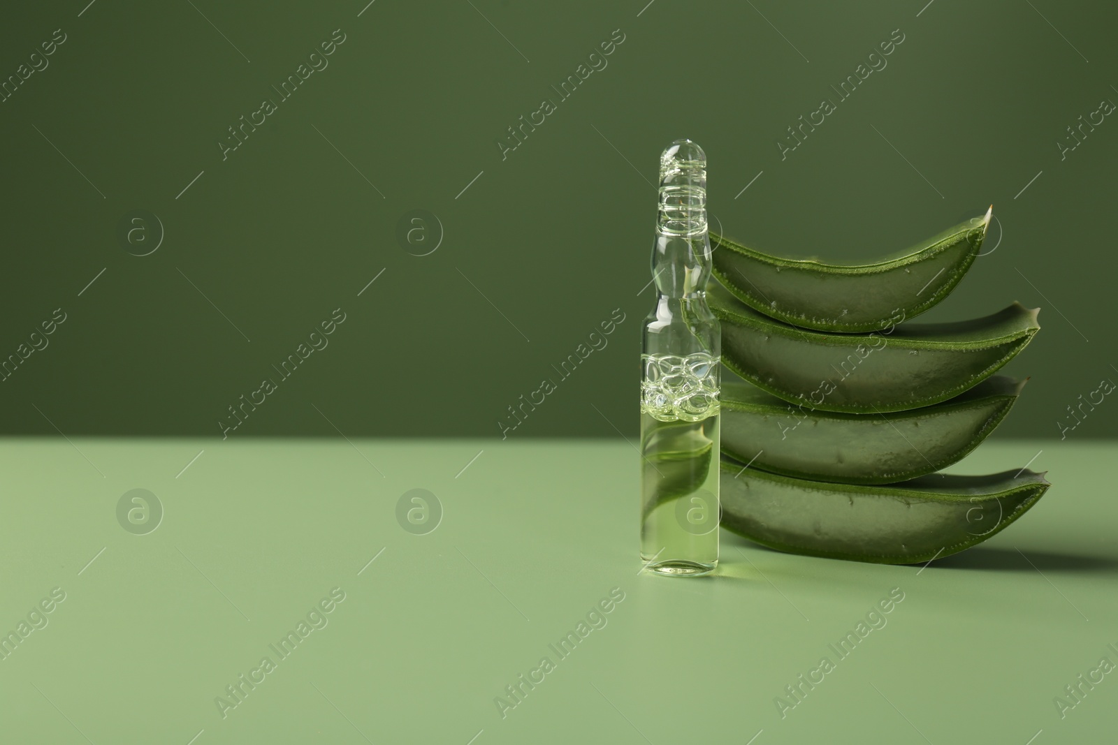 Photo of Skincare ampoules with extract of aloe vera and cut green leaves on color background. Space for text