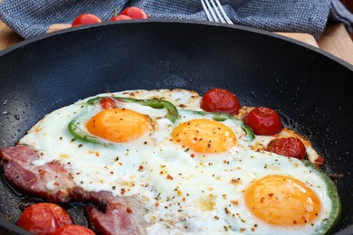 Delicious fried eggs with bacon, tomatoes and pepper in frying pan, closeup