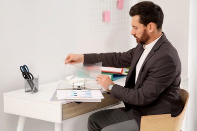 Businessman putting punched pocket into folder at white table in office