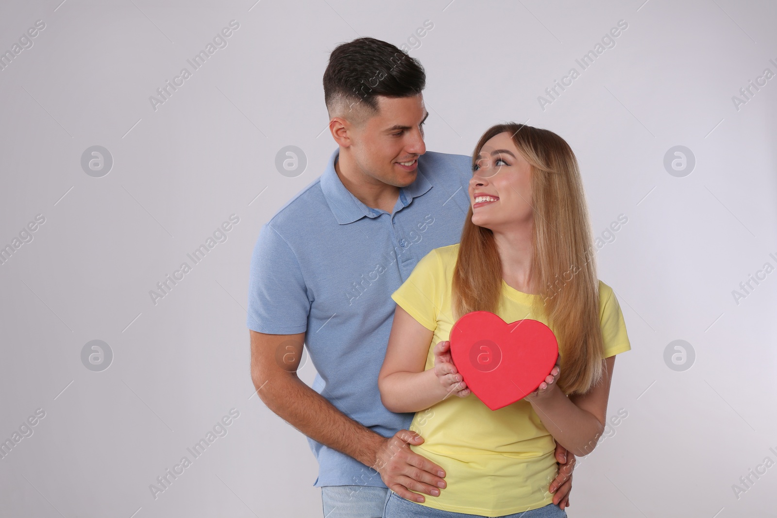 Photo of Man surprising his girlfriend with gift on grey background. Valentine's day celebration