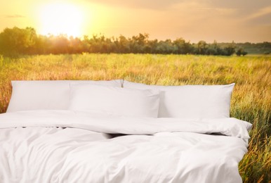 Comfortable bed with soft pillows in field at sunset