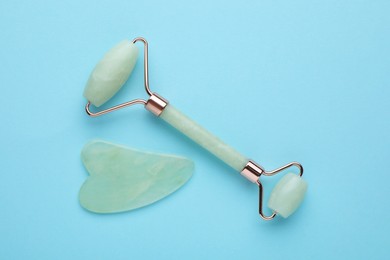 Photo of Jade gua sha tool and facial roller on light blue background, flat lay