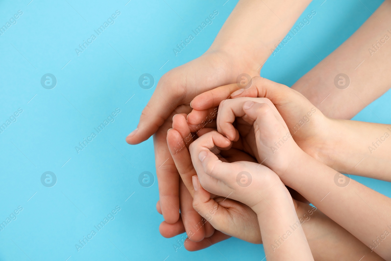 Photo of Happy family holding hands on light blue background, top view. Space for text