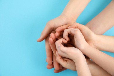 Happy family holding hands on light blue background, top view. Space for text