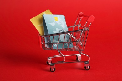 Photo of Small metal shopping cart with credit cards on red background