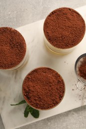 Delicious tiramisu in glasses and mint on grey textured table, top view