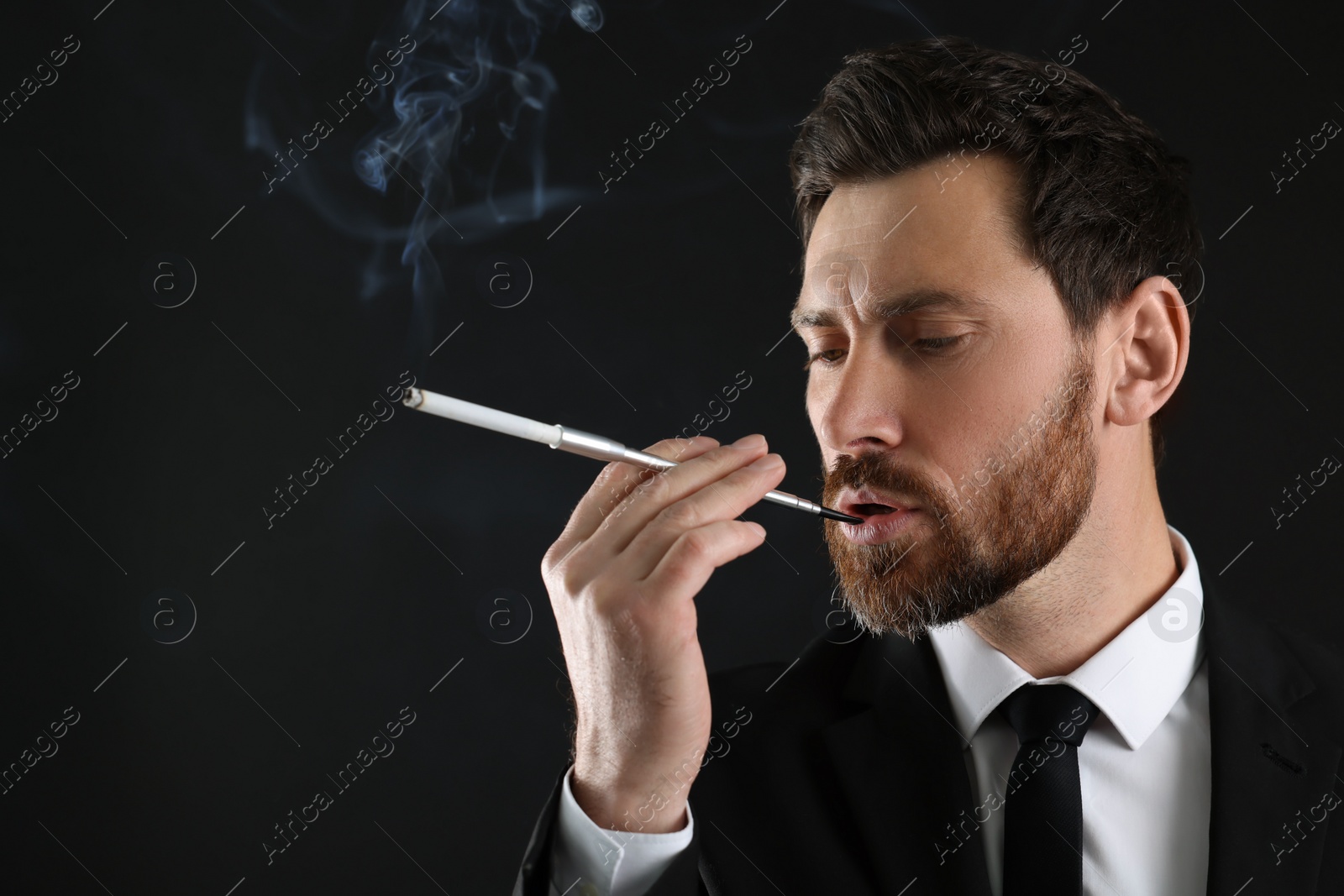 Photo of Man using long cigarette holder for smoking on black background, space for text