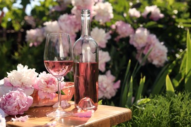 Photo of Bottle and glass of rose wine near beautiful peonies on wooden table in garden. Space for text