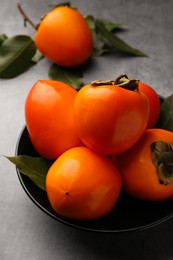 Photo of Delicious ripe persimmons in bowl on light gray table