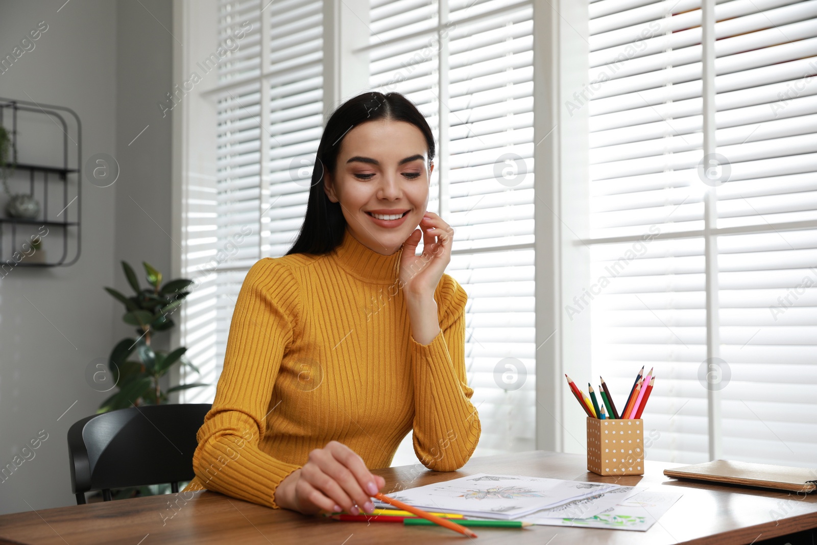 Photo of Young woman coloring antistress page at table indoors