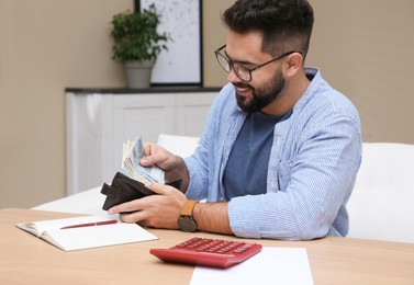 Photo of Young man putting money into wallet at table indoors